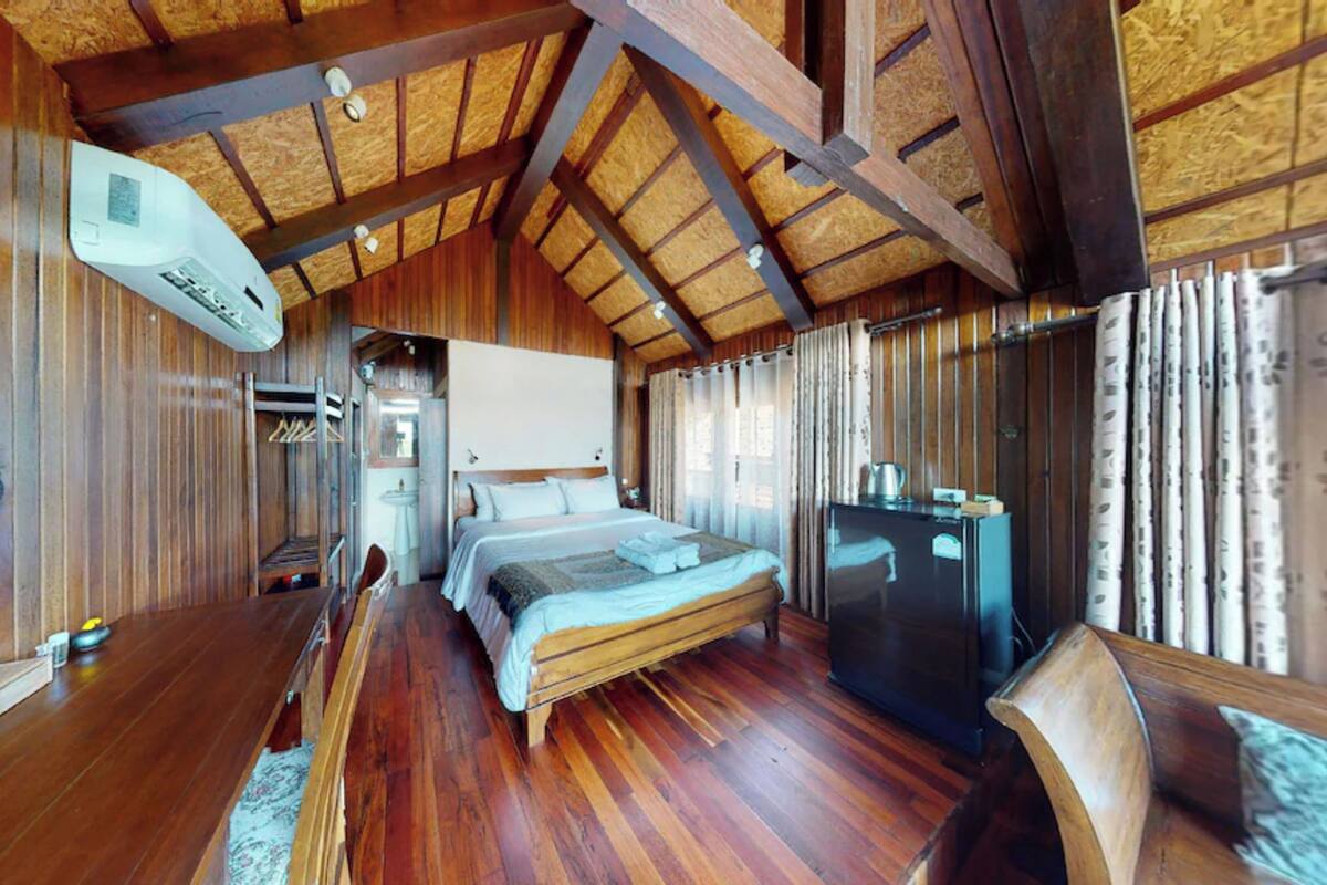 A wooden room with a bed, a desk, and a refrigerator.