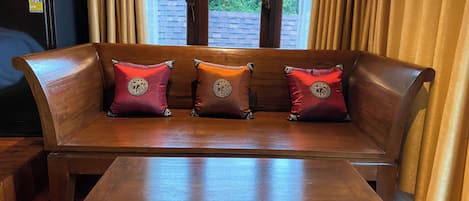 A wooden bench with three cushions, a wooden table in front, and a window with curtains.