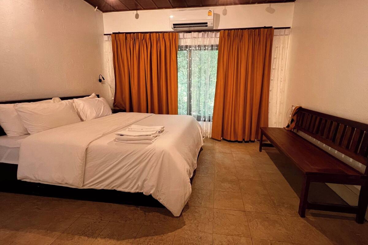A bedroom with a bed, a bench, and a window with curtains.