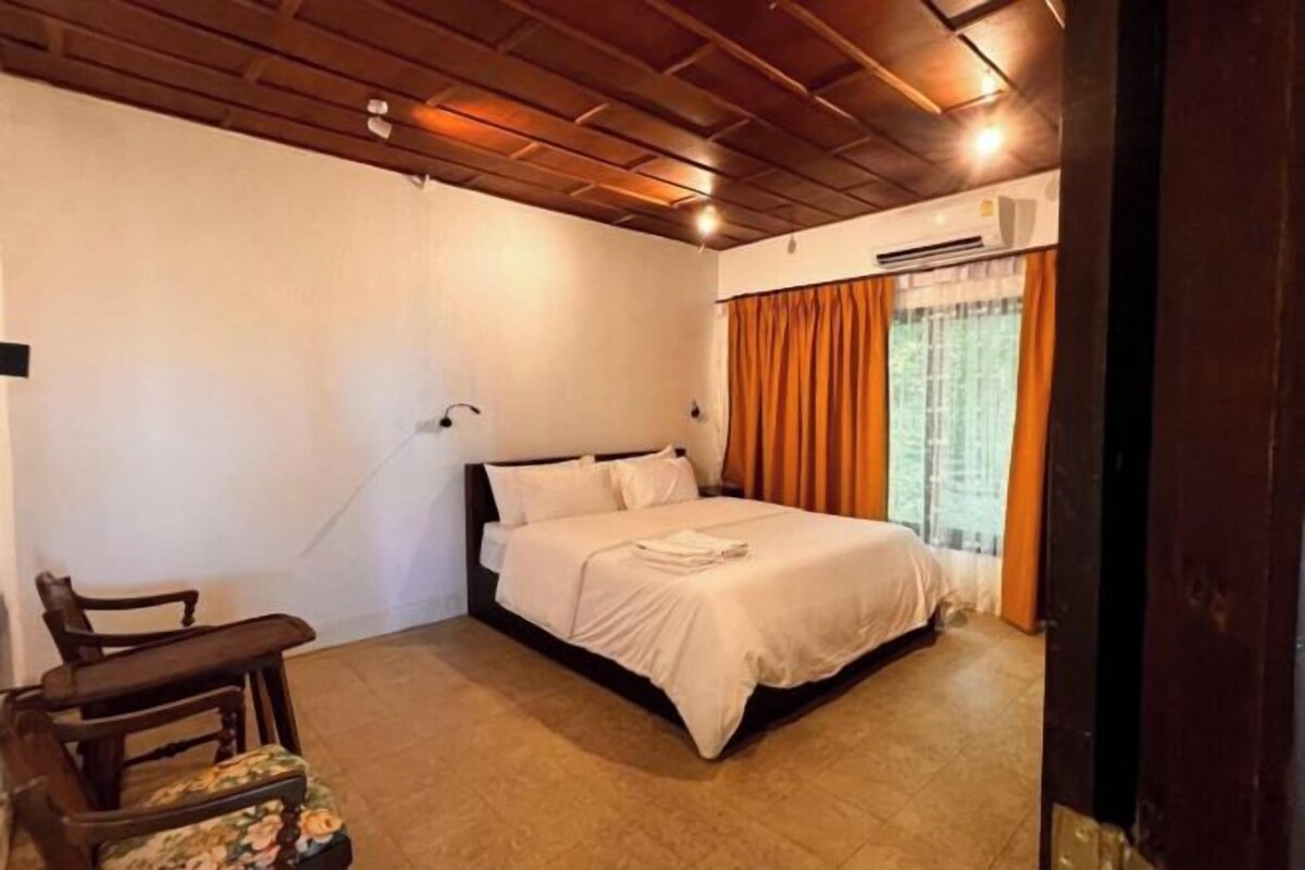 Une chambre à coucher comprenant un lit, une chaise, une fenêtre avec des rideaux et un appareil de climatisation.