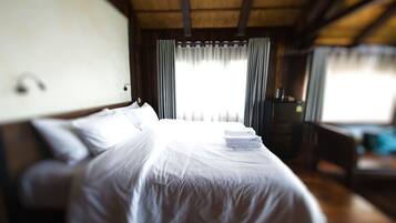 A bed with white linens, a bedside table, and a window with curtains.