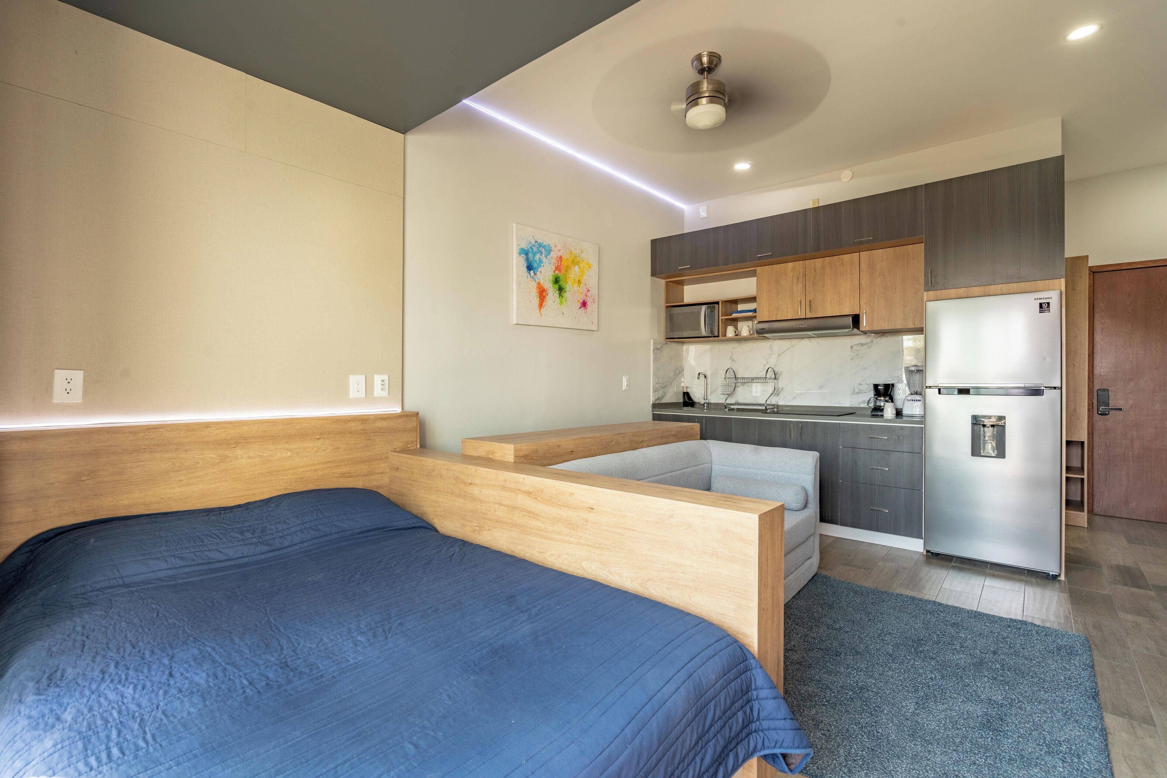 A modern bedroom with a large bed, a small kitchenette, and a ceiling fan.