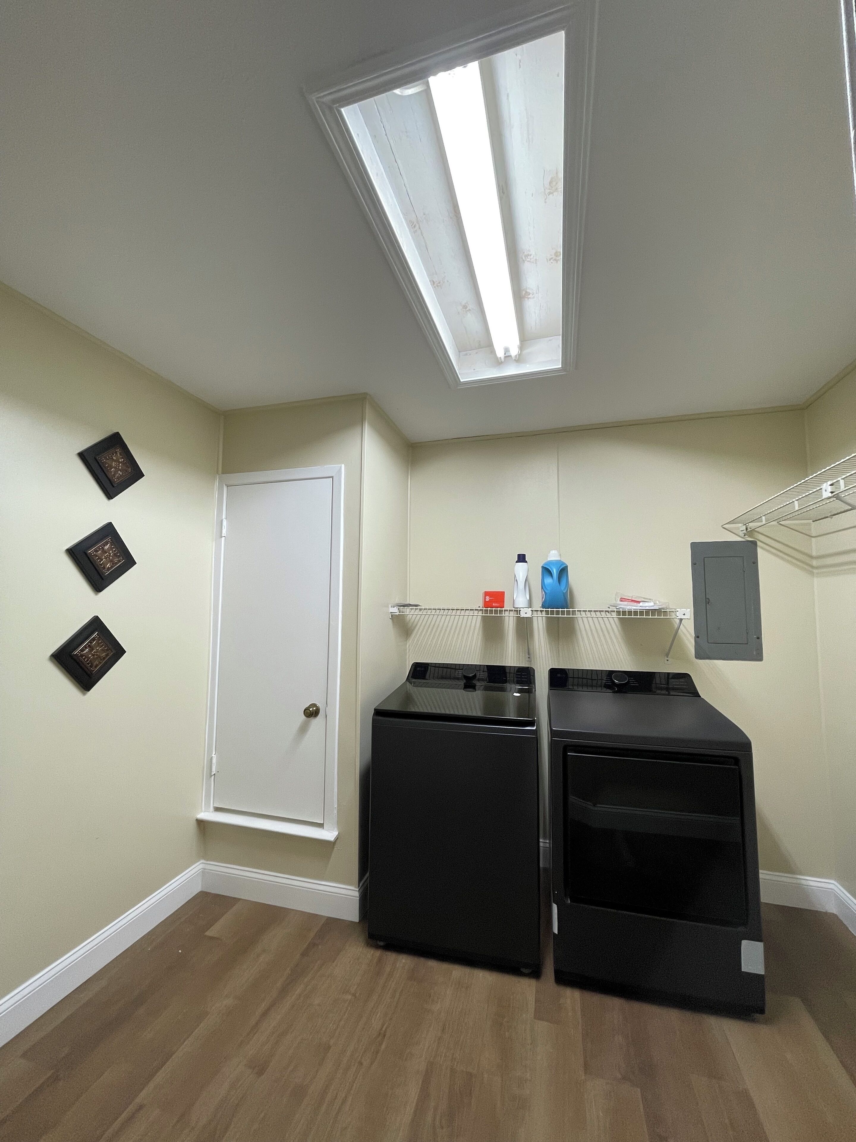 A laundry room with a skylight, a door, and three framed pictures on the wall.