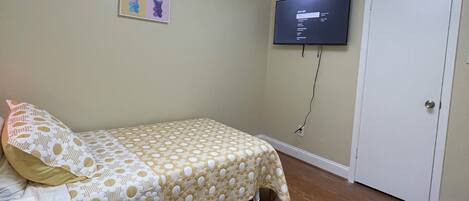 A bedroom with a bed, a ceiling fan, a TV, and a door.