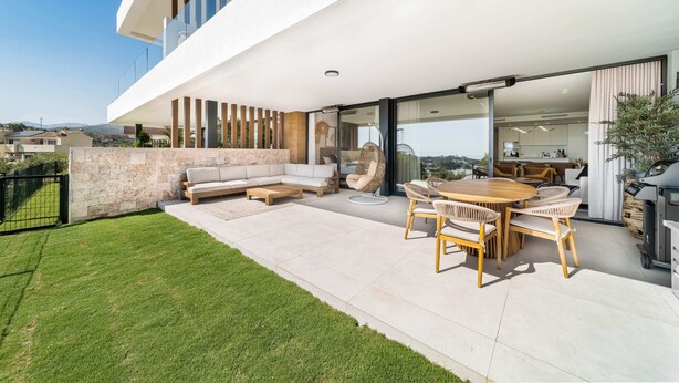 Un espace de vie extérieur moderne comprenant un mur en pierre, un canapé, une table à manger avec des chaises et un barbecue.