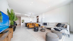 Un salon moderne avec un canapé, des poufs, une table basse et un téléviseur posé sur un meuble en bois.