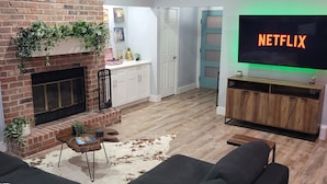 A living room with a brick fireplace, a flat-screen TV, and a cowhide rug. - 4bd 3ba - Pool / HotTub/ Arcade/ Theater/ PingPong/ Foosball (Pflugerville)