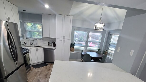 A modern kitchen with white cabinets, a stainless steel refrigerator, a dishwasher, and a large island with bar stools. - 4bd 3ba - Pool / HotTub/ Arcade/ Theater/ PingPong/ Foosball (Pflugerville)