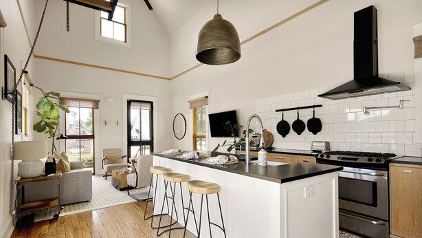 A modern kitchen with a large island, bar stools, a hanging pot rack, and a large window.
