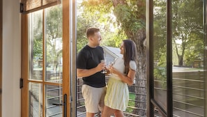 A couple standing by a glass door with a view of a tree and a building in the background.