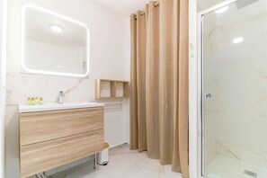 Bathroom features a white sink, lighted vanity, and glass shower door.