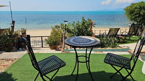 A patio with two chairs and a table, overlooking a beach and the sea.
