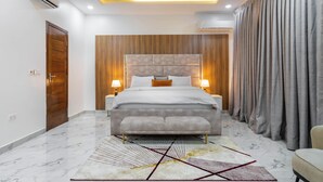 A modern bedroom with a large bed, bedside lamps, a wooden accent wall, and a patterned rug. - Ocean view Luxurious 2 bedroom apartment on Lekki phase 1. Close to all beaches (Lekki)