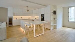 Una cocina moderna con muebles blancos, una isla central con taburetes, electrodomésticos integrados y un amplio ventanal que proporciona luz natural.