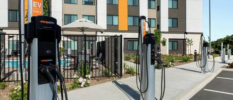 A row of EV charging stations in front of a modern building with a pool and outdoor seating.
