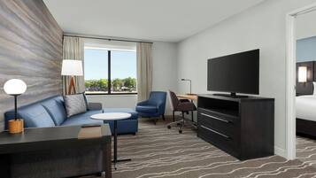 A modern hotel room with a sofa, a small table, a TV, a desk, and a bed.