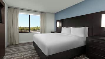 A hotel room with a large bed, a nightstand, a dresser, and a window with curtains.