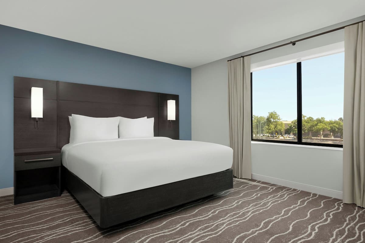 Een moderne hotelkamer met een groot bed, een nachtkastje, een raam met gordijnen en uitzicht op de omgeving.