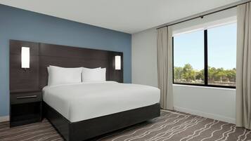 Habitación de hotel moderna con una cama grande, una mesita de noche, una ventana con cortinas y vistas al exterior.