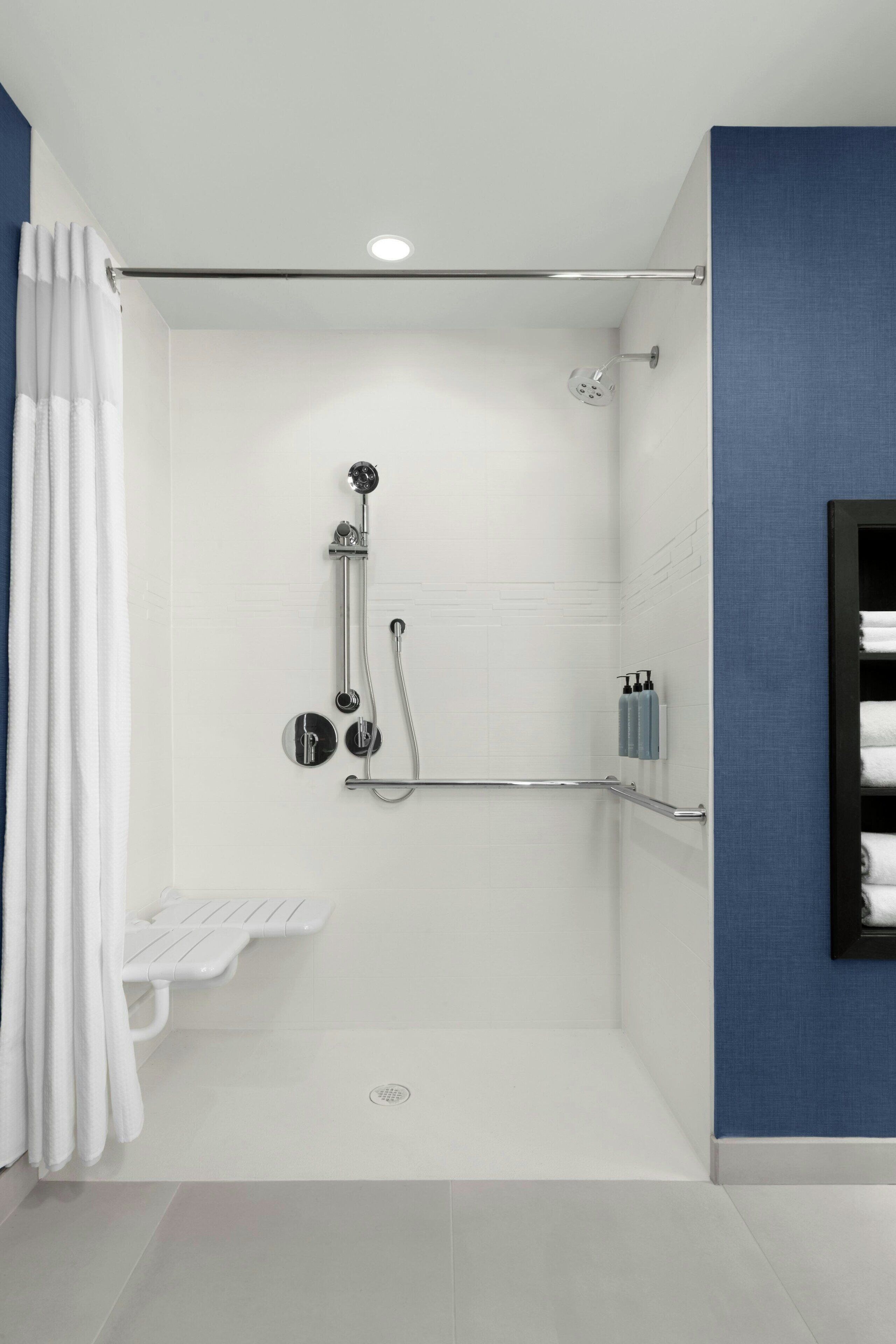 A modern bathroom with a walk-in shower, grab bars, a towel rack, and a toilet.