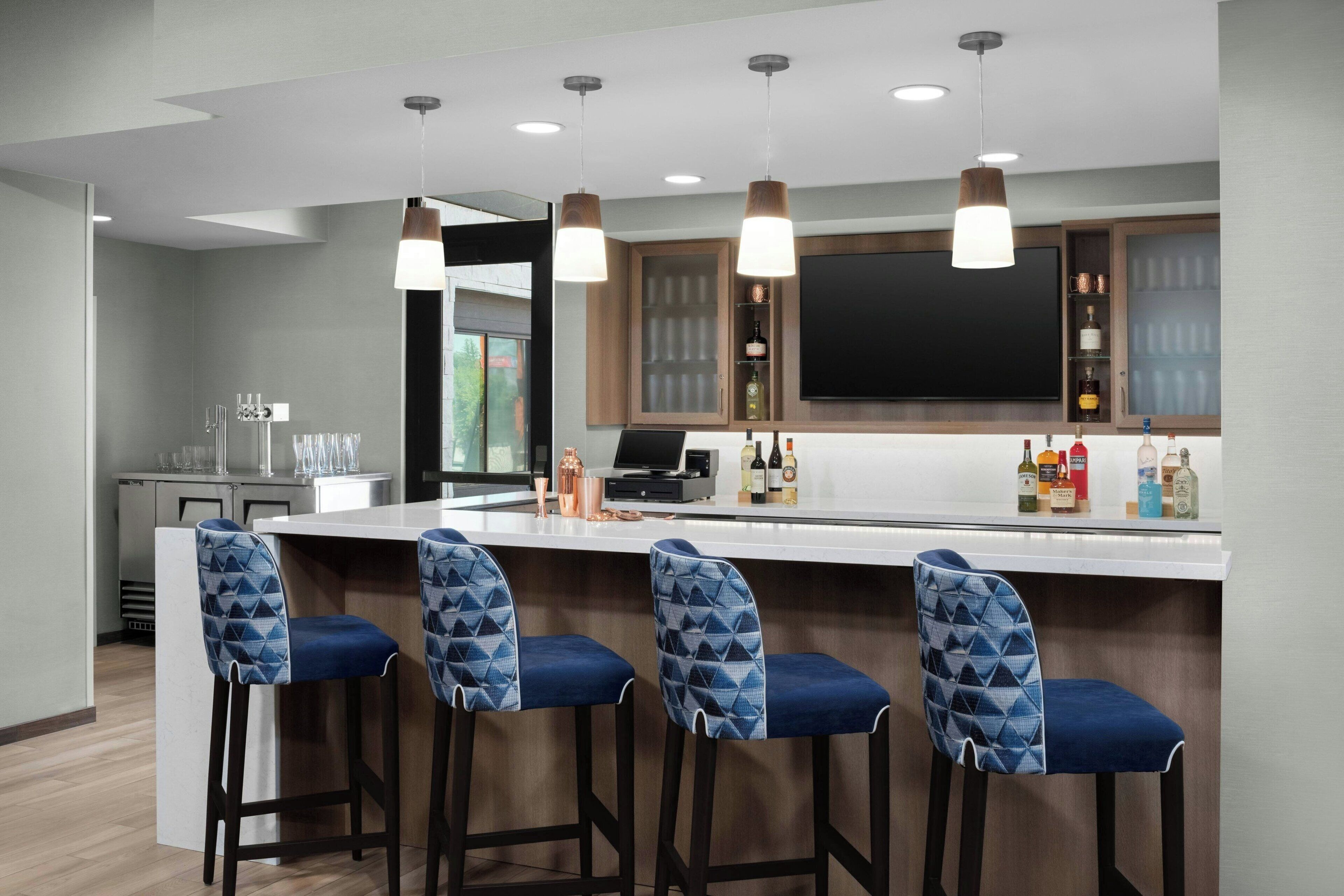 A modern kitchen with a bar area, featuring a large island with bar stools, pendant lighting, and a flat-screen TV above the counter.