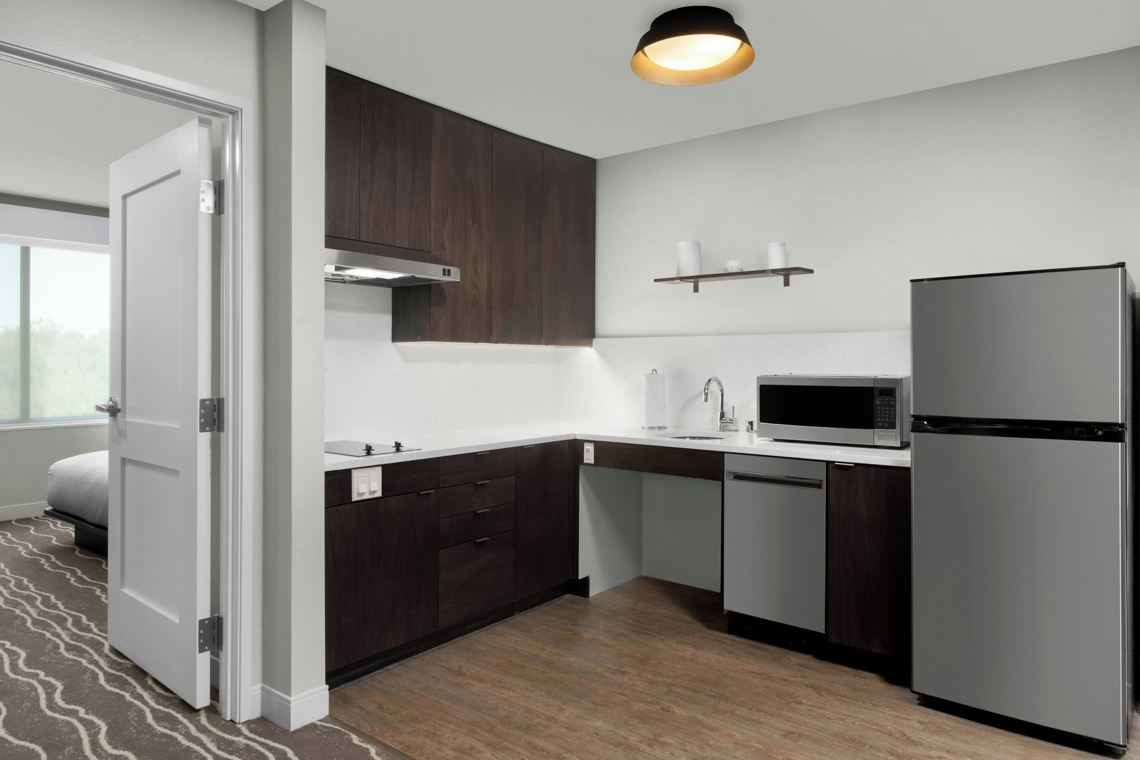 A modern kitchen with dark wood cabinets, a stainless steel refrigerator, a microwave, and a built-in dishwasher.