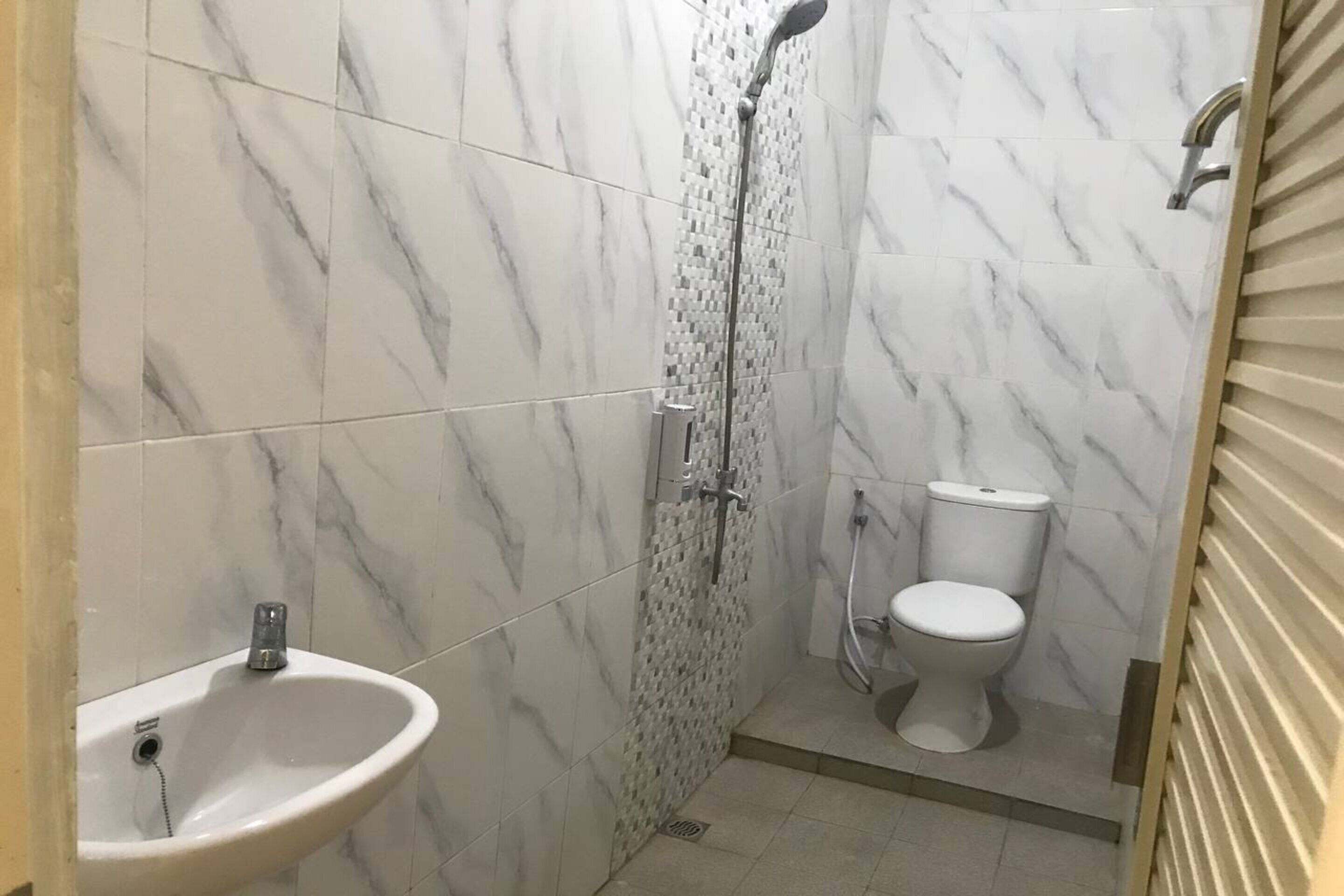A bathroom with a shower, toilet, and sink, all tiled with a marble pattern.