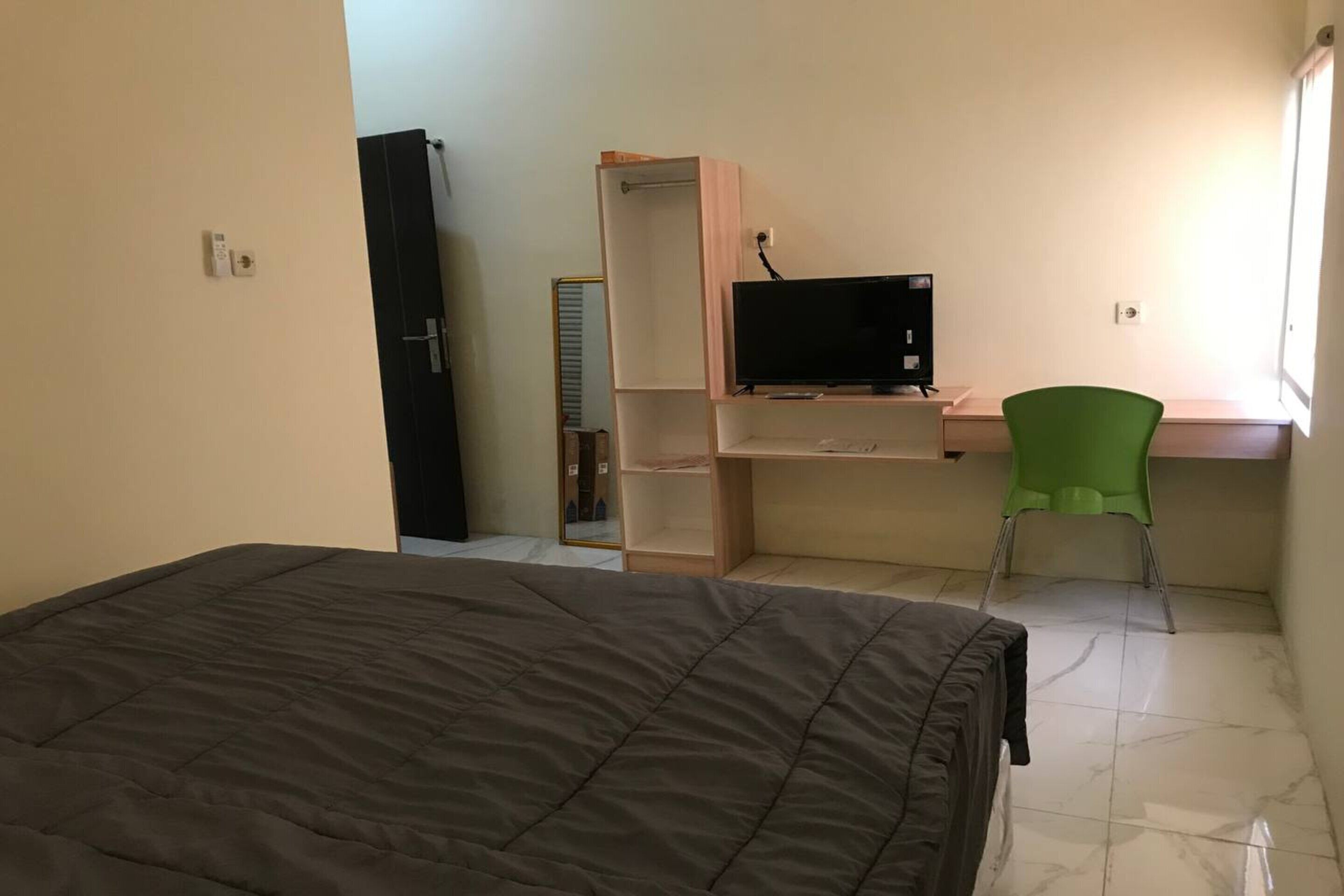 Um quarto com cama, uma escrivaninha com computador, uma cadeira verde e um guarda-roupa.