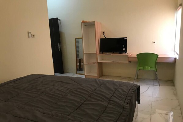 A bedroom with a bed, a desk with a computer, a green chair, and a wardrobe. - Capital O 94128 The Bale Teras't (Colomadu)