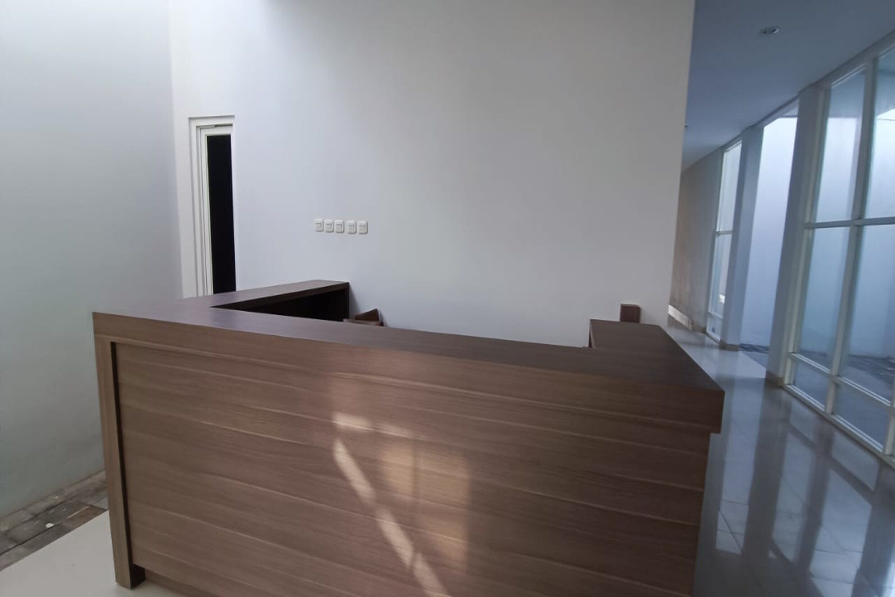 A modern reception desk with a wooden finish, a door to a room, and large windows allowing natural light.
