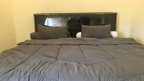Una cama con colcha gris oscuro y dos almohadas, cabecera negra y mesita de noche blanca.