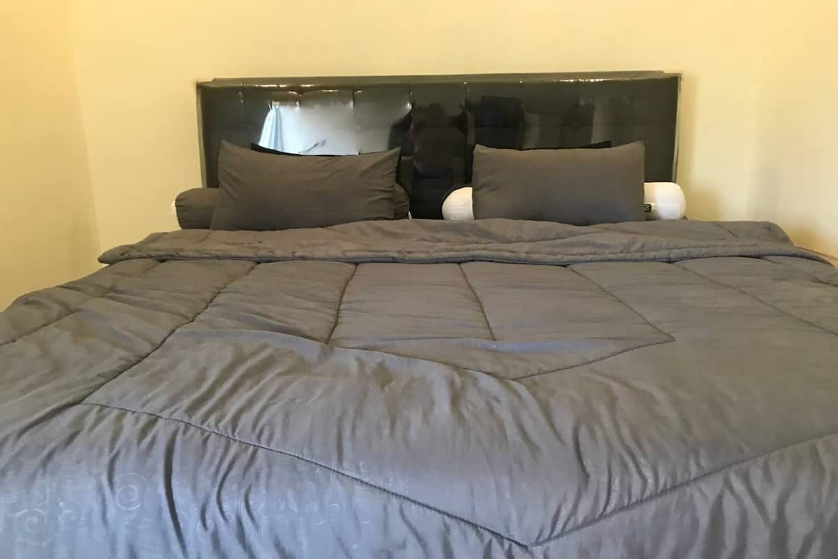 Un lit avec une couette gris foncé et deux oreillers, une tête de lit noire et une table de chevet blanche.