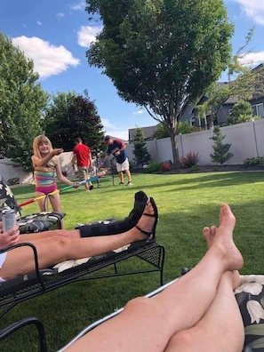 A backyard with a lawn, a metal chair, and a person lying down.