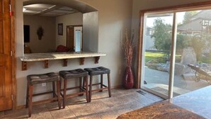 A kitchen with a built-in island, two bar stools, a vase, and a sliding glass door leading to a patio. - Gorgeous Executive Home - Hot Tub, Gym, Theatre, and More! (Spokane)
