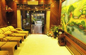 A hotel lobby with a reception desk, a seating area with yellow sofas, a large mural, and a wooden floor. - Tamcoc Lights Hotel (Nam Hoa Lu)