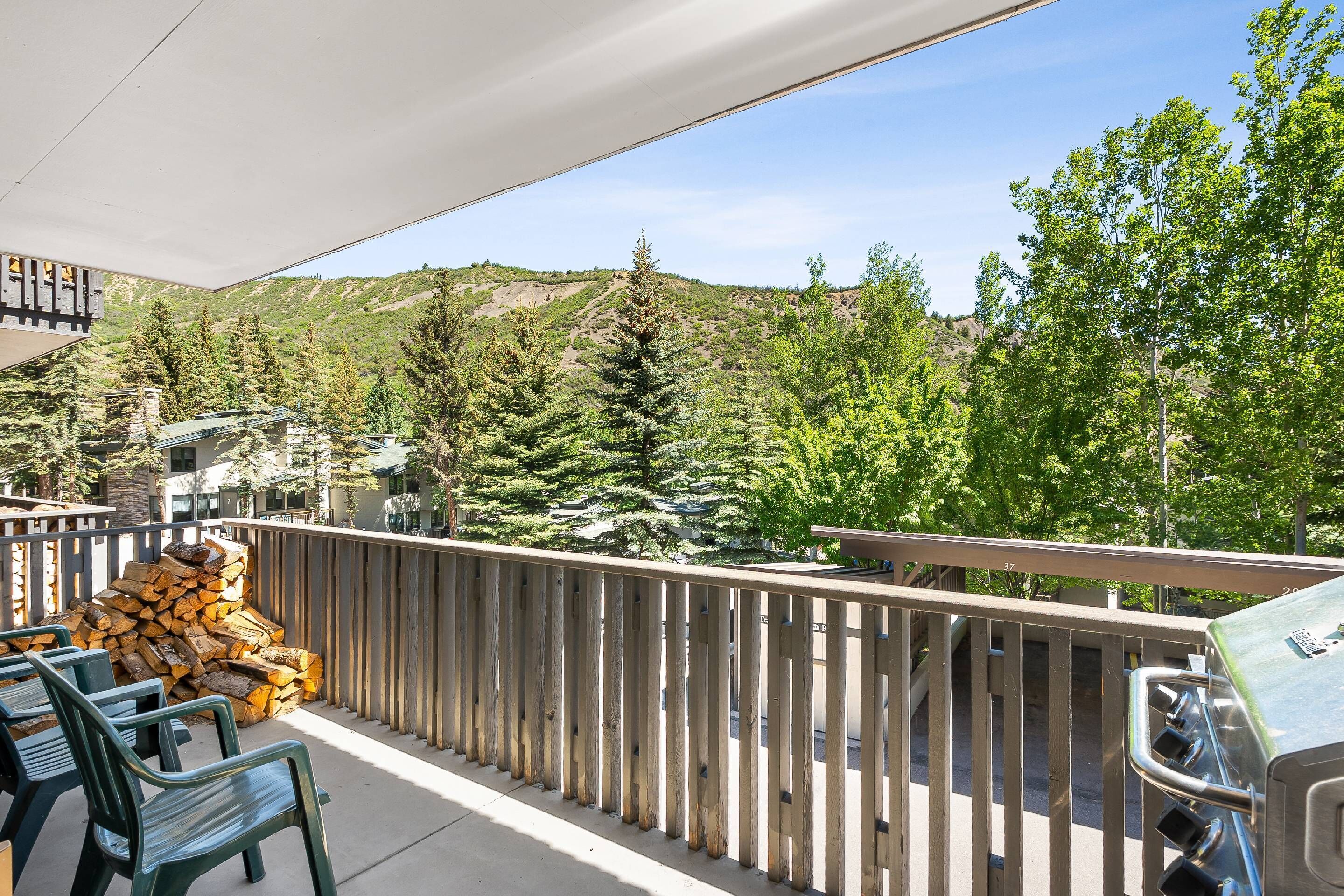 A balcony with a grill, chairs, and stacked firewood.
