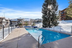 A swimming pool with a metal ladder, surrounded by a metal fence, with buildings and snow in the background. - Special VRBO Rates - Walk to Trails & Shops! Snowmass Condo w/ Hot Tub (Snowmass Village)