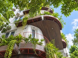 Un edificio de varios niveles con balcones, rodeado de abundante vegetación.