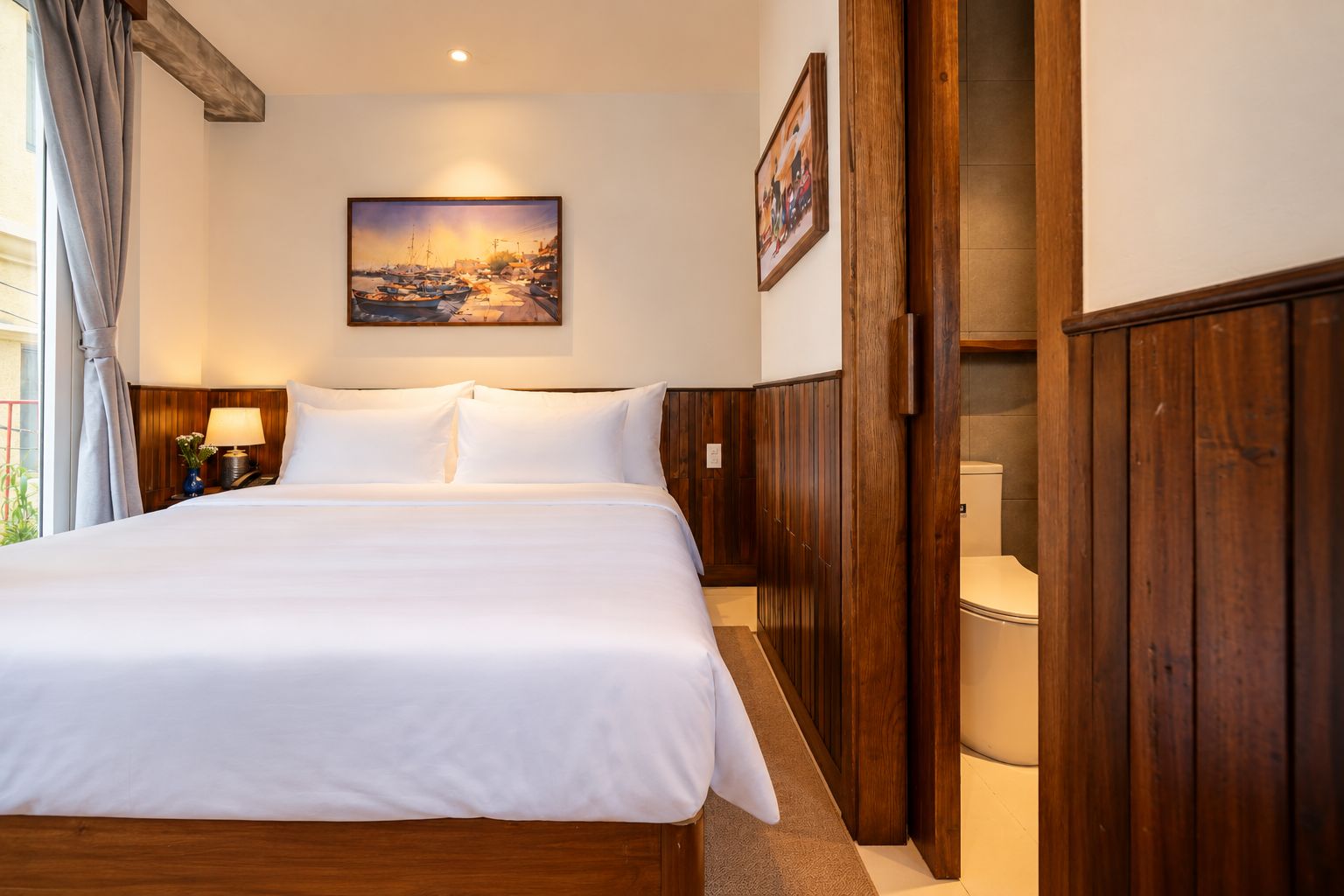 Een hotelkamer met een groot bed, een houten hoofdeinde, een schilderij aan de muur en uitzicht op zee.