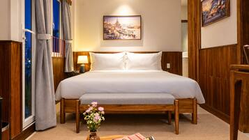 Ein Hotelzimmer mit einem hölzernen Bett, einem Nachttisch mit Lampe, einer Blumenvase und einem Fenster mit Vorhängen.