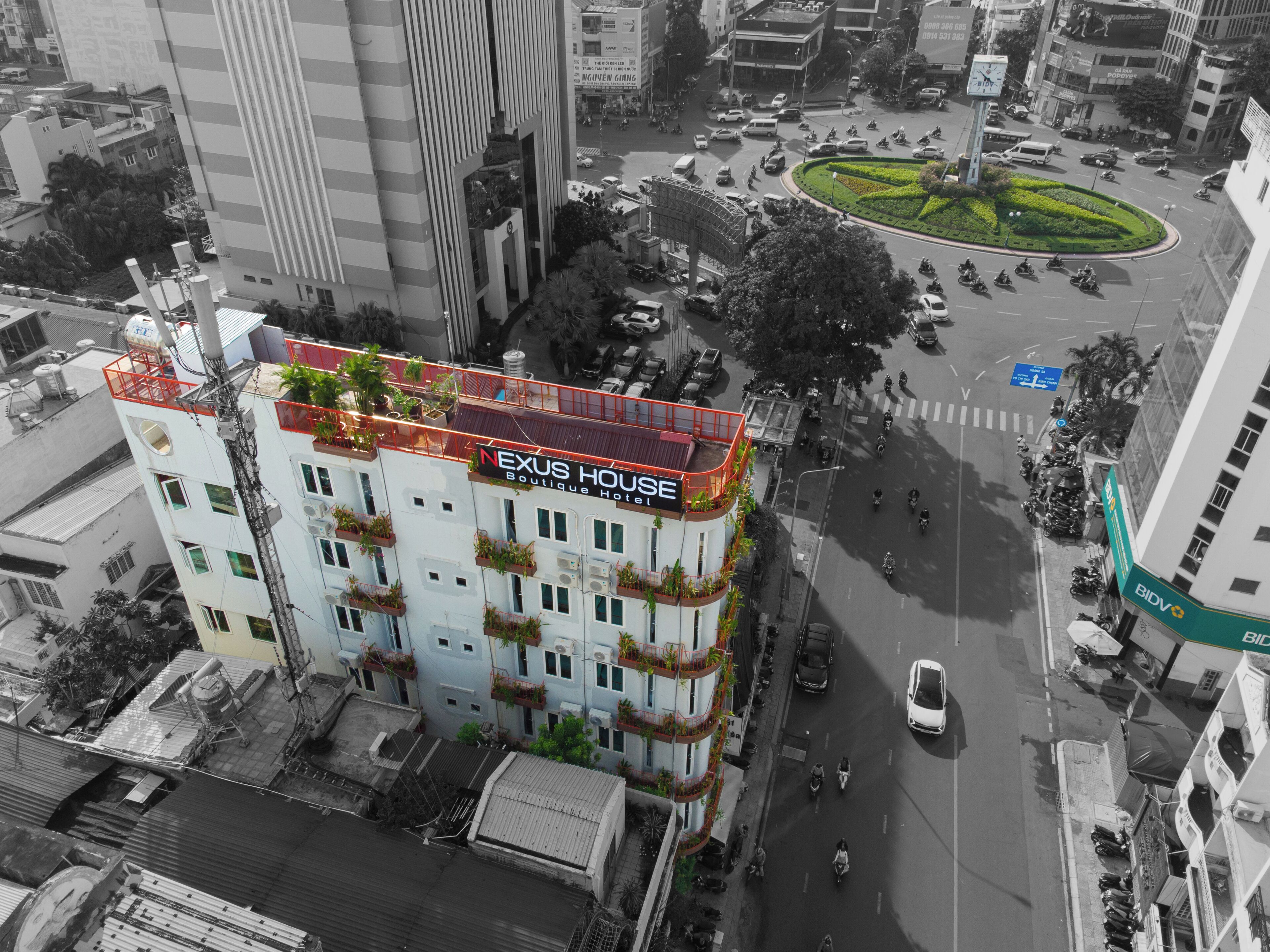 A multi-story building with balconies, a rooftop garden, and a sign reading "NEXUS HOUSE Boutique Hotel".