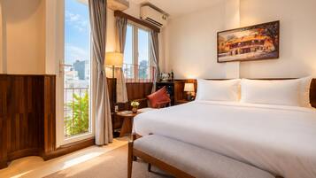 Quarto de hotel com uma cama grande, uma escrivaninha com cadeira, janela com cortinas e um quadro na parede.