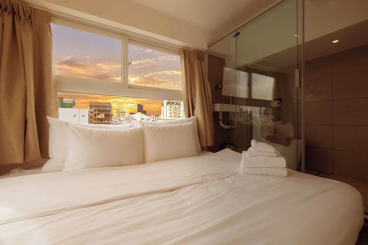 A hotel room with a large bed, a glass shower, and a city view.