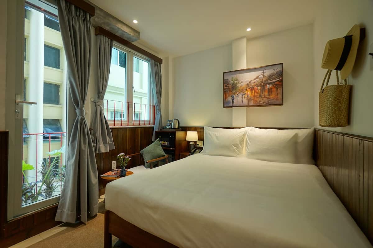 A hotel room with a large bed, a desk with a lamp, a chair, and a window with curtains.