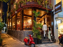 Entrada de un hotel con una scooter roja estacionada afuera, una escalera que conduce a la entrada y un letrero que dice 'Nexus House Boutique Hotel'.