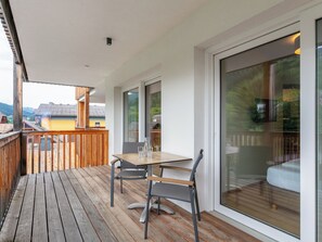 Un terrazzo in legno con tavolo e sedie, ampie porte scorrevoli in vetro e vista su montagne e edifici.