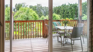 Una terraza de madera con una mesa y sillas, con vista a un paisaje verde exuberante.