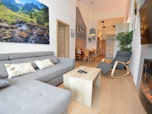 Ein modernes Wohnzimmer mit grauem Sofa, einem Holztisch und einem Essbereich mit Holzsesseln und einem Tisch.