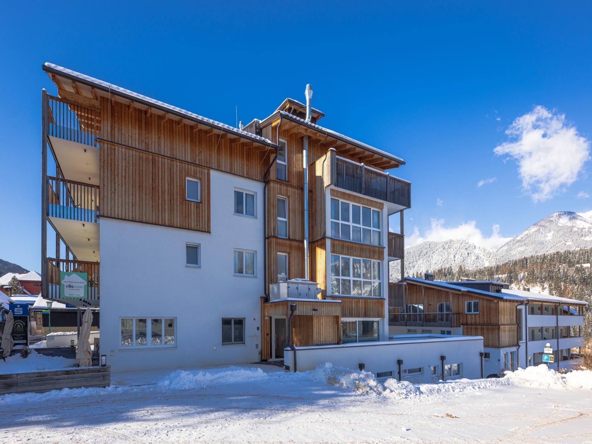 A multi-story hotel with wooden exterior, large windows, and a snowy mountain backdrop.