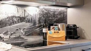 Et køkken med en moderne komfur, en kaffemaskine og en flaske vin på bordet.